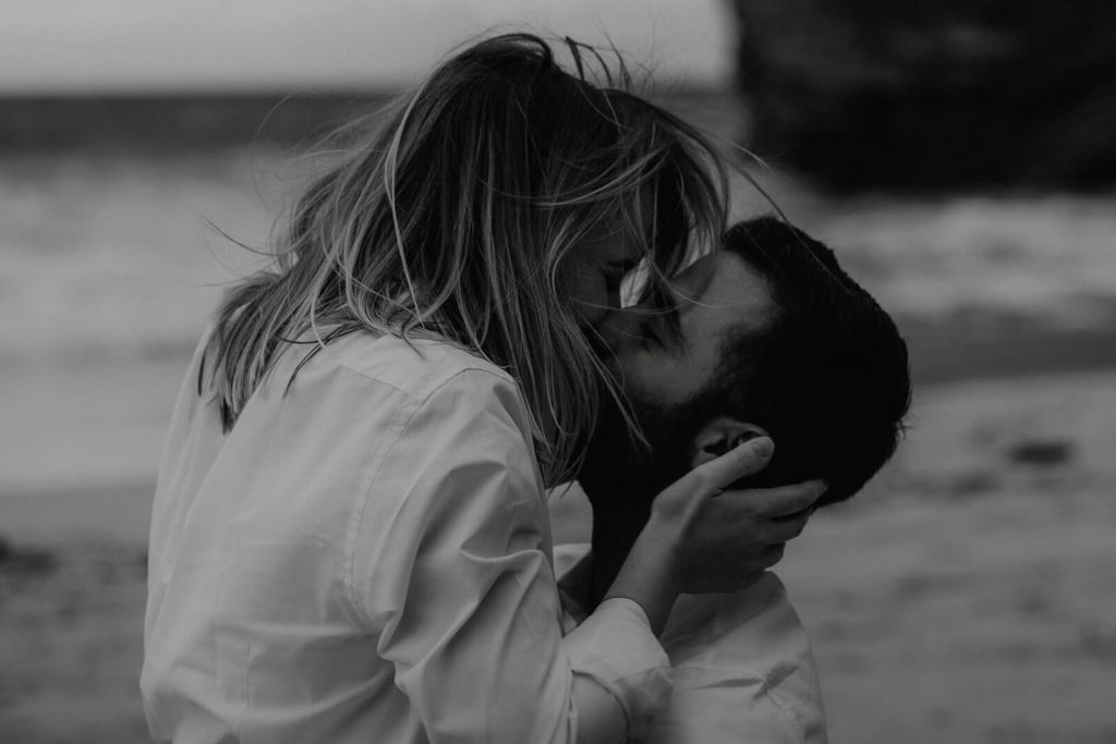 photo d'un couple qui s'embrasse passionnellement à la plage dans le pays basque. Ses cheveux volent au vent. La photo est prise par Gaétane Glize, photographe de couple et de fiançailles dans les landes et le pays basque.