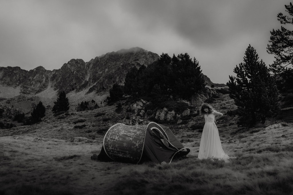 Photo d'une mariée qui sort de sa tente dans les Pyrénées après avoir passé une nuit à bivouaquer en montagne. Elle met sa robe de mariée pour faire une séance photo de couple aventurière, un elopement pendant lequel ils vont symboliquement se marier. Photo prise par la photographe Gaétane Glize.
