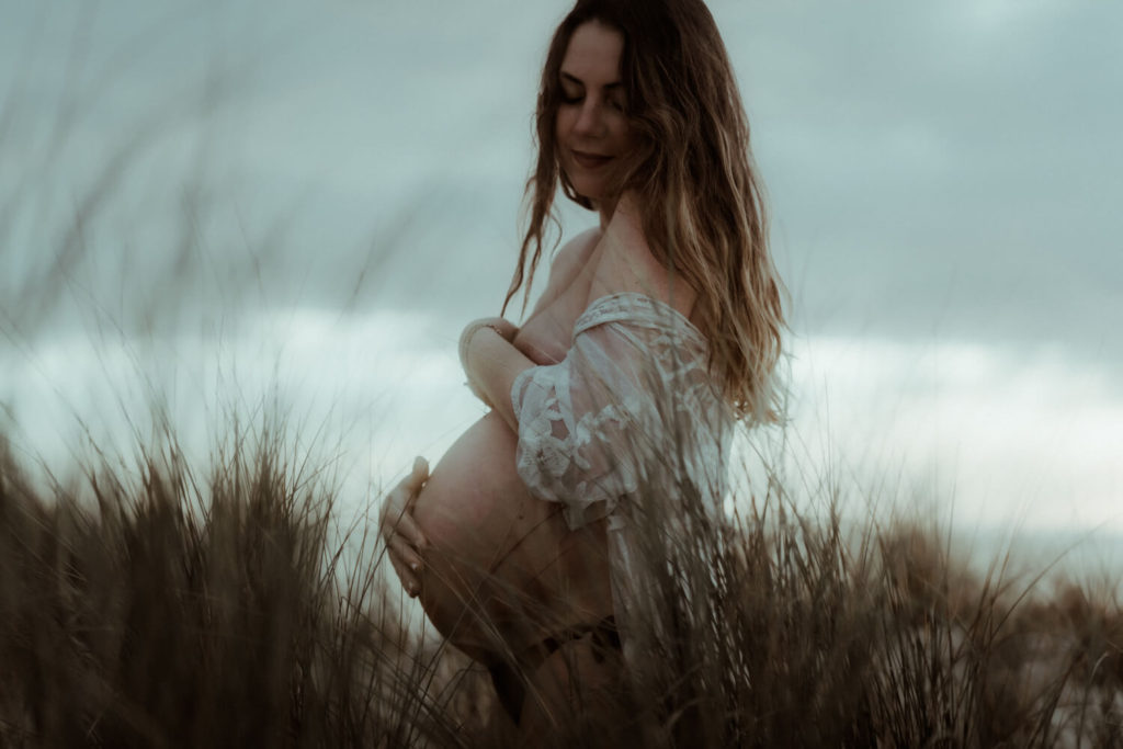 la femme enceinte sourit en pensant à son bébé qui va naître bientôt. Un moment de tendresse capturé par la photographe Gaétane Glize pendant la séance photo grossesse dans les landes.
