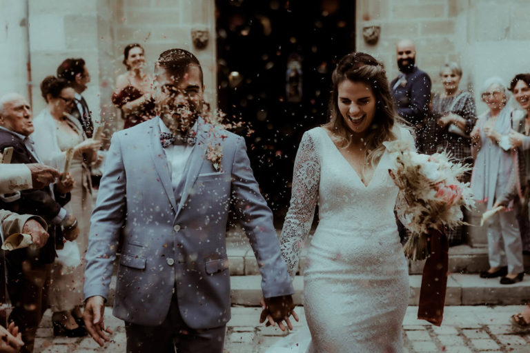 Les mariés sortent de l'église sous une pluie de pétales de fleurs après leur cérémonie de mariage dans les Landes. Un moment de joie capturé sur le vif par la photographe de mariage Gaétane Glize.