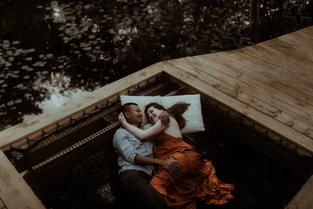 Un moment de complicité entre un couple qui attend un enfant. Ils sont tous les deux allongés au bord d'un étang dans les landes et rigolent ensemble. Un moment capturé dans une cabane en bois pendant leur séance photo grossesse.