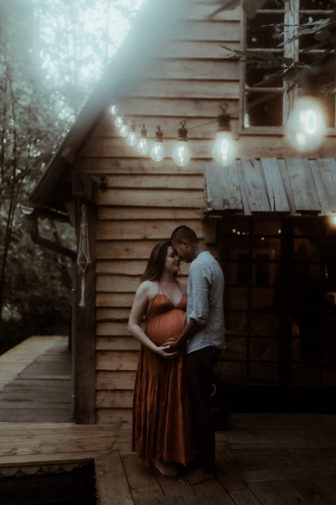 Le couple partage un moment de tendresse pendant leur séance photo grossesse dans un chalet en bois dans les landes.