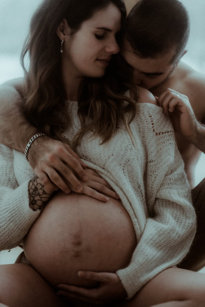 l'homme embrasse délicatement l'épaule de sa femme enceinte pendant leur séance photo de grossesse