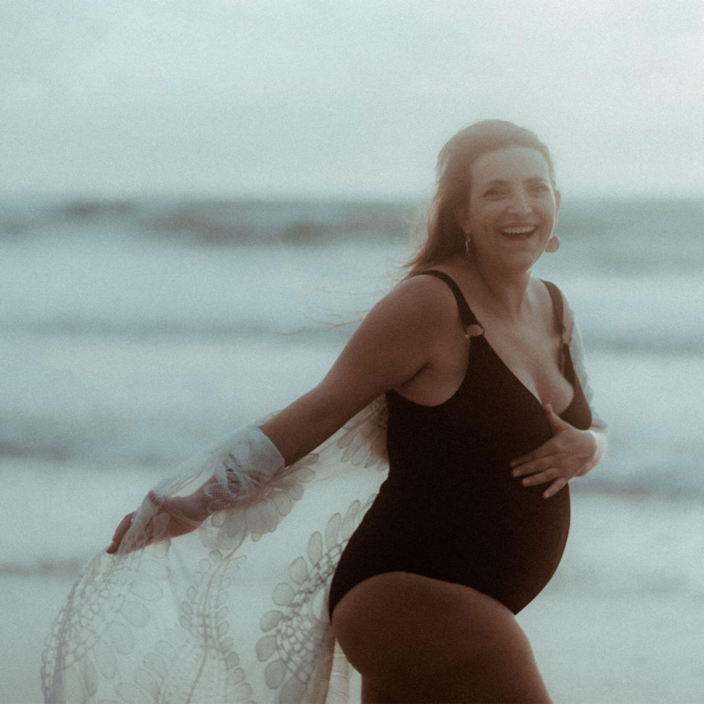Une femme enceinte rigole aux éclats pendant sa séance photo de grossesse sur la plage à seignosse dans les Landes au coucher de soleil.